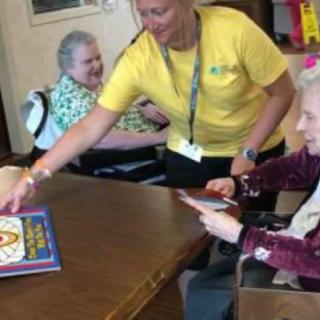 A caregiver assists elderly individuals in an activity session at a nursing home.
