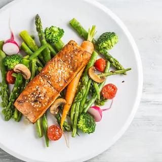 A delicious plate of grilled salmon served with fresh vegetables including asparagus, broccoli, radishes, and cherry tomatoes.