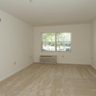 An empty room with beige carpet, a window, and an air conditioner.
