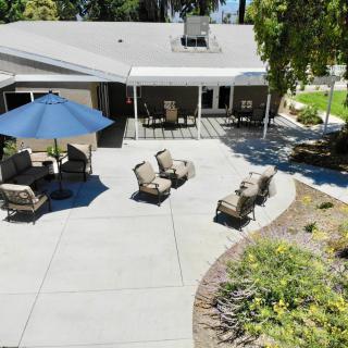 A well-furnished backyard patio with seating and an umbrella, surrounded by a landscaped garden.