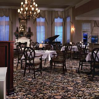 An elegant dining room with a chandelier, a grand piano, and neatly set tables.
