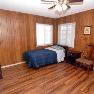 A cozy bedroom with wood paneling, featuring a single bed with blue bedding, a hardwood floor, and a ceiling fan.