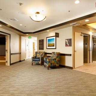 A modern hallway featuring elevators, comfortable seating, and decorative wall art.