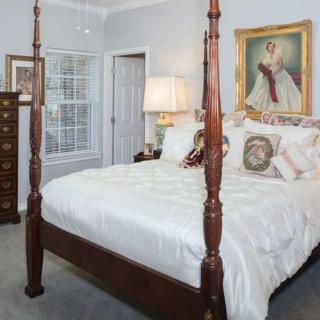 A cozy bedroom featuring a traditional four-poster bed, decorative pillows, and an elegant painting on the wall.