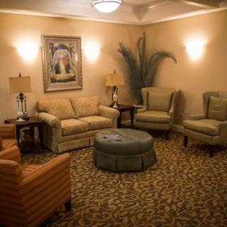 A cozy living room with sofas, chairs, and a central ottoman, warmly lit by lamps.