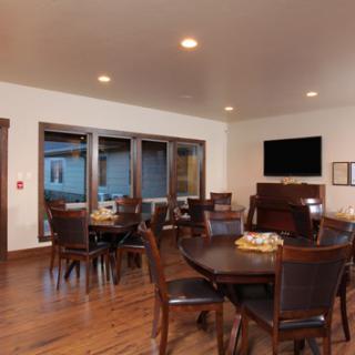 A modern dining room with wooden tables and chairs, featuring a television and large windows.