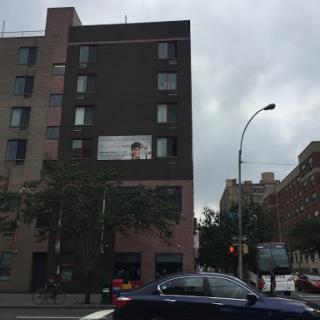 A view of a modern urban building with an advertisement on the side, set against a cloudy sky.