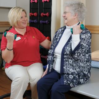 A healthcare professional guides a senior woman in an exercise session using dumbbells for strength training.