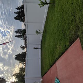 A backyard with a white fence, grassy lawn, and a cloudy sky.