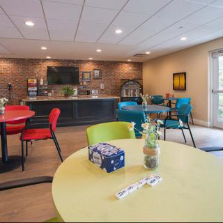 A modern lounge with colorful seating, tables, a television, and a coffee station.