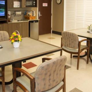 A communal kitchenette and seating area with tables, chairs, a television, and decorative flowers.
