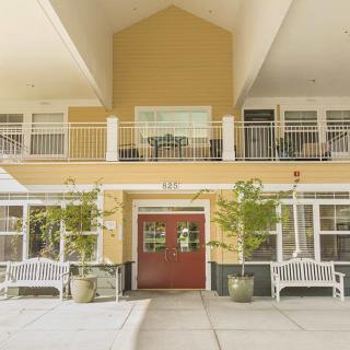 A two-story building entrance with a red door, benches, and potted plants.
