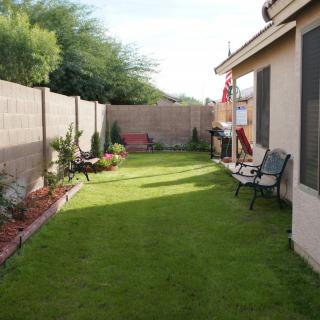 A neatly landscaped backyard with a green lawn, bordered by garden beds and a fence, featuring outdoor seating for relaxation.