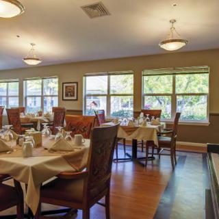 A well-lit dining room with neatly arranged tables and chairs, featuring large windows and elegant lighting.