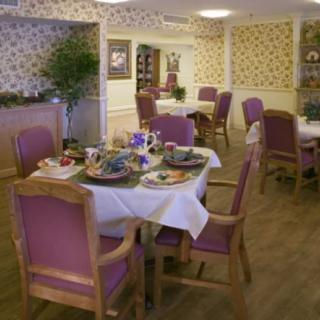 A cozy dining area with tables set for a meal, featuring purple chairs and floral wallpaper.