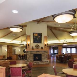 A cozy dining area with wooden furniture and a central fireplace, illuminated by ceiling lights.