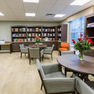 A cozy library space with bookshelves, tables, and chairs, adorned with flower arrangements.