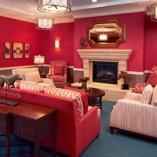 A warmly decorated living room with red walls, elegant furniture, and a central fireplace.