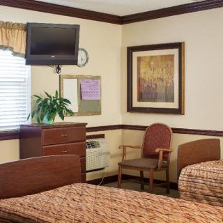 A hospital room with two beds, a TV, and seating area.