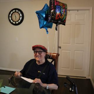 An elderly person celebrates a birthday with balloons indoors.