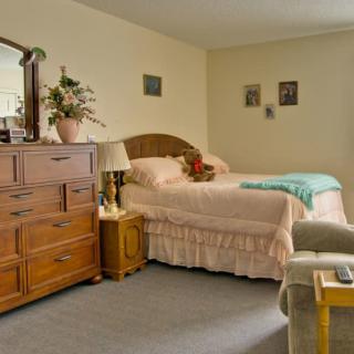 A cozy bedroom with a neatly made bed, dresser, and decorative items.