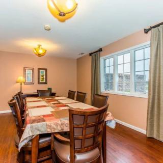A spacious dining room with a large table and chairs, featuring warm lighting and window curtains.