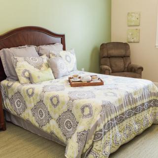 A cozy bedroom with neatly arranged bedding and a comfortable chair.