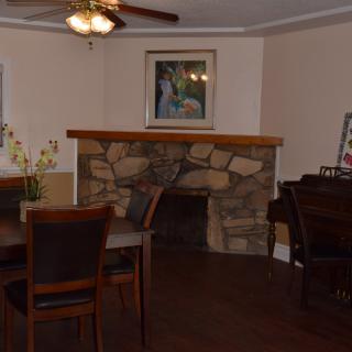 A cozy living room with a stone fireplace, dining table, and a piano.