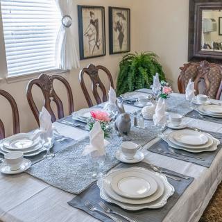 An elegantly set dining table with plates, cutlery, and decorations in a well-lit room adorned with artwork.