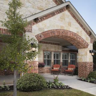 A cozy porch with brick and stone accents, featuring outdoor seating and surrounding greenery.