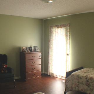 A cozy bedroom with green walls, featuring a dresser and a chair by the window.