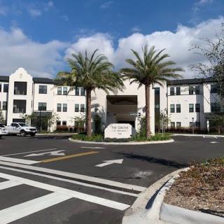 A modern building with palm trees at the entrance under a partly cloudy sky.