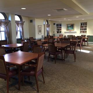A spacious dining area with multiple tables and chairs, well-lit by natural light from the windows.
