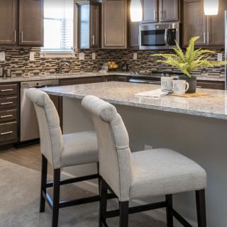 Modern kitchen with a central island and bar stools, featuring sleek cabinets and a stylish backsplash.