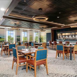 A modern restaurant interior with neatly arranged tables and chairs, featuring stylish lighting and a bar area.