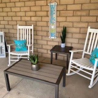 A cozy patio area with white rocking chairs and a coffee table, adorned with plants and turquoise pillows.