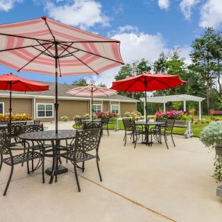 An inviting outdoor patio area with red umbrellas and metal furniture, set in a garden under a bright blue sky.