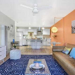 A stylish and vibrant open-concept living space featuring a modern sofa, colorful accents, and a well-equipped kitchen.