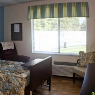 A cozy, well-lit room with a bed, chairs, and a large window.