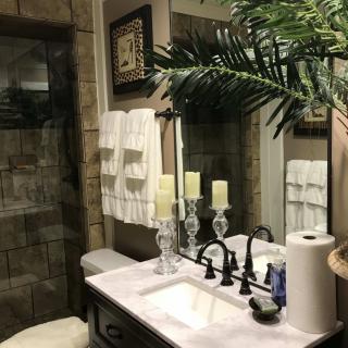 A well-decorated bathroom with a sink and mirror, featuring candles, towels, and a glass shower door.