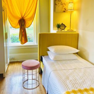 A cozy bedroom with vibrant yellow decor, featuring a single bed and a small stool by the window.