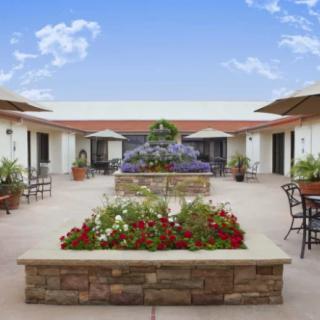 A serene courtyard with vibrant flower beds and outdoor seating under a clear blue sky.