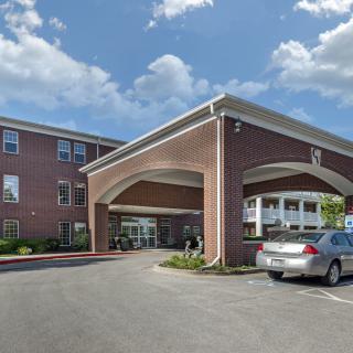 A brick building with an entrance canopy and a parked car under a partly cloudy sky.