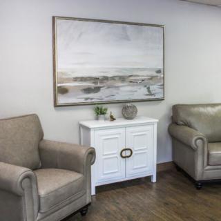 A cozy living room with two armchairs, a white cabinet, and a landscape painting on the wall.