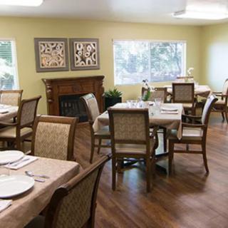 A well-lit dining room with neatly arranged tables and chairs, featuring elegant decor and large windows.
