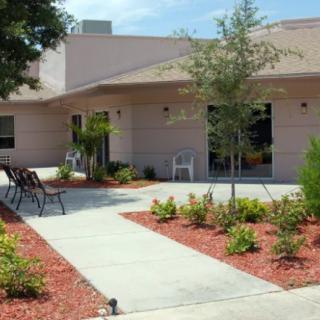A well-maintained garden with a pathway leading to a building, featuring outdoor seating and various plants.