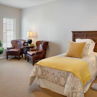 A cozy bedroom with a single bed and elegant armchairs by the window.