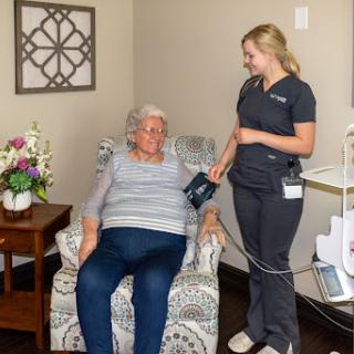 A nurse checks the blood pressure of an elderly patient in a comfortable indoor setting.