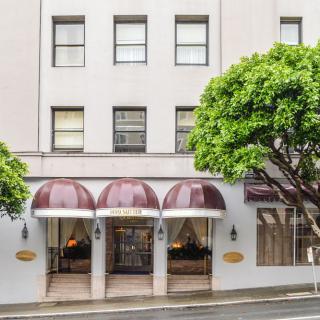 Facade of a hotel with maroon awnings and trees on the sidewalk.