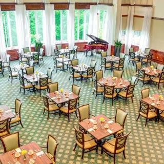 An elegant dining room with neatly arranged tables and a grand piano by the window.